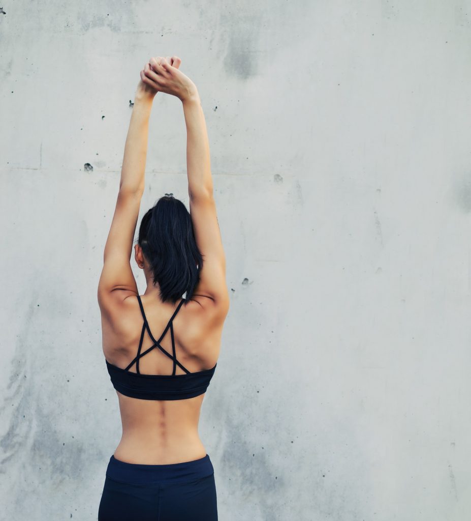 Žena otočená chrbtom, ktorá si naťahuje chrbát a ruky. Žena cvičí jogu.