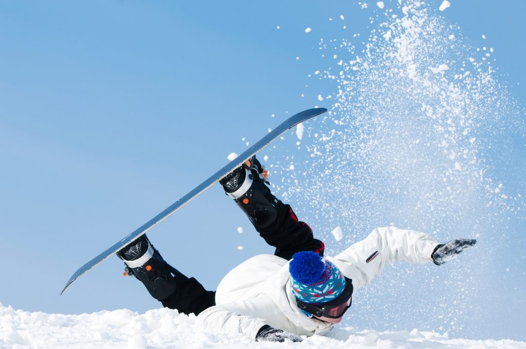 Muž na snowboarde padajúci na zasnežený svah.
