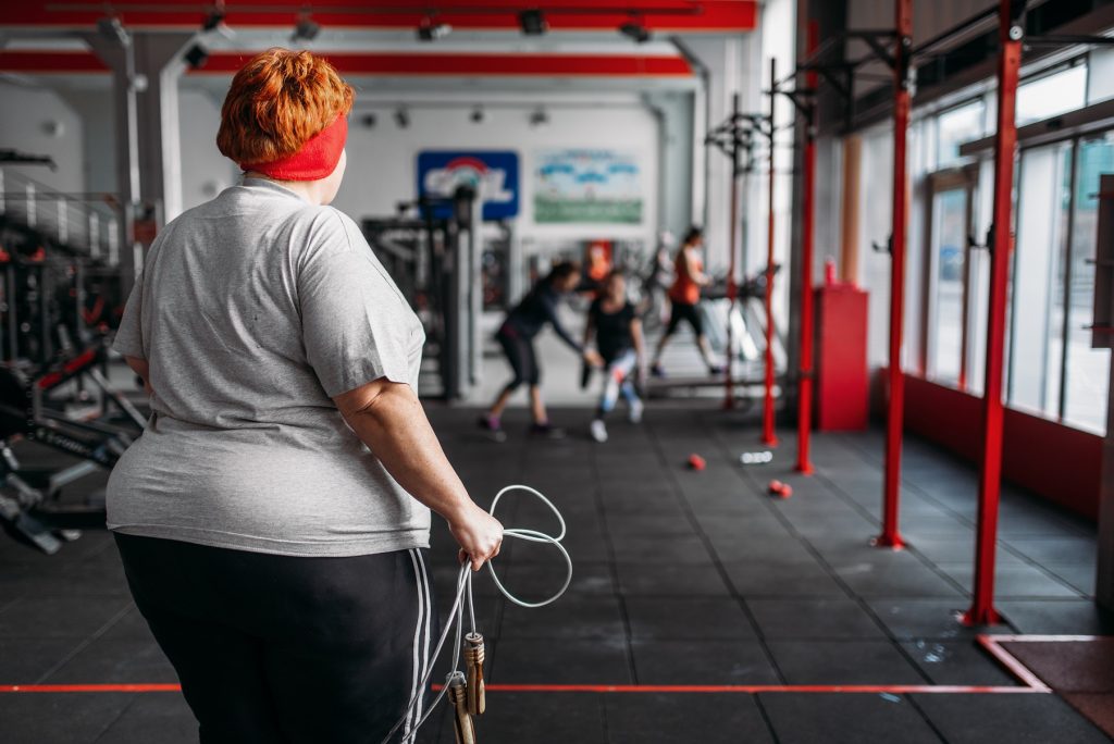 Obézna žena so švihadlom v ruke vo fitness centre.